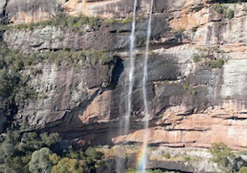 Powerful waterfall cascading down a rugged cliff face, with a vibrant rainbow arching in the mist below.