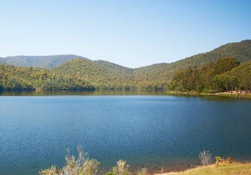 Calm blue lake surrounded by lush green hills and dense forest, under a clear blue sky