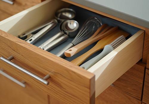 Neatly organized kitchen drawer with wooden utensils, metal spoons, and a whisk, showcasing clean and functional storage