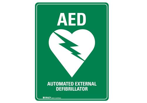 Green sign with white text and a heart symbol featuring a lightning bolt, indicating the location of an Automated External Defibrillator (AED).