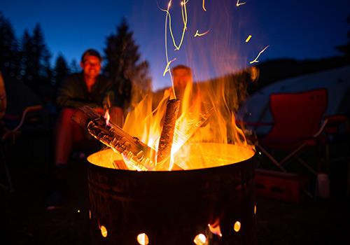 A warm, glowing campfire burning brightly at night, with people sitting around it and tents in the background