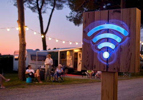 Wooden sign with a glowing blue Wi-Fi symbol at King River Caravan Park, Wangaratta Accommodation, surrounded by campers enjoying the evening outdoors under string lights